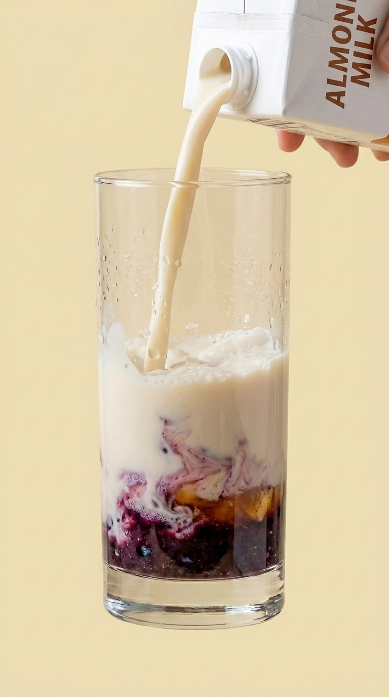 Almond milk being poured from a carton into the glass over the berry-honey-lemon paste