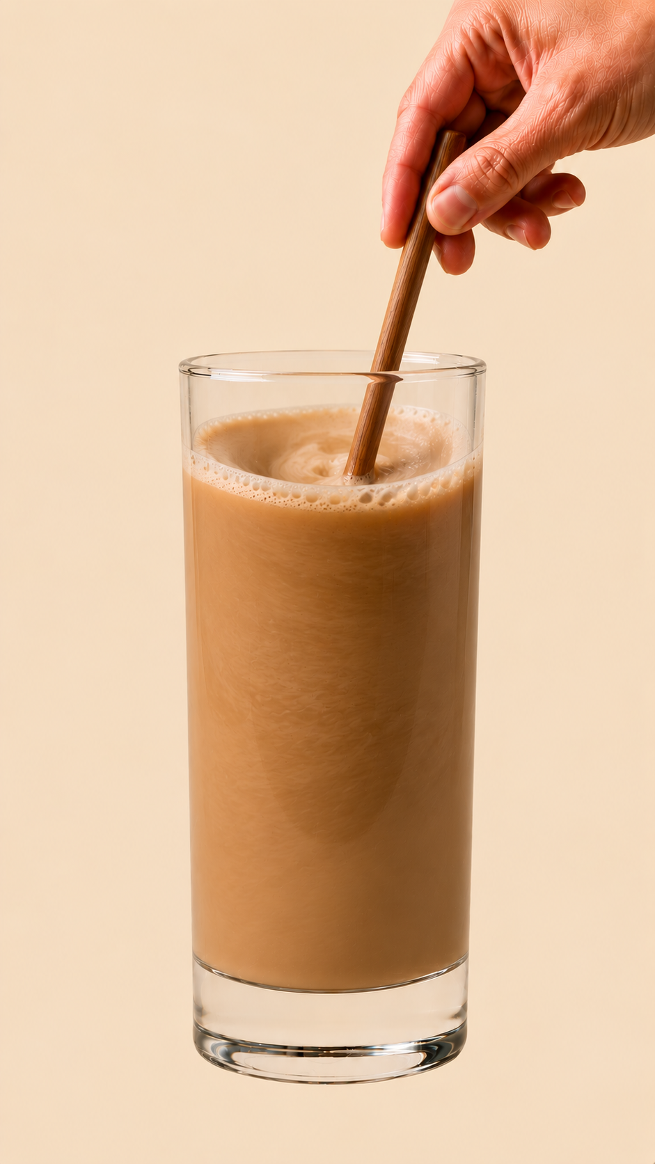 Finished latte in a tall clear glass, frothy creamy top with a sprinkle of cinnamon dust, a small wooden stirrer resting against the rim